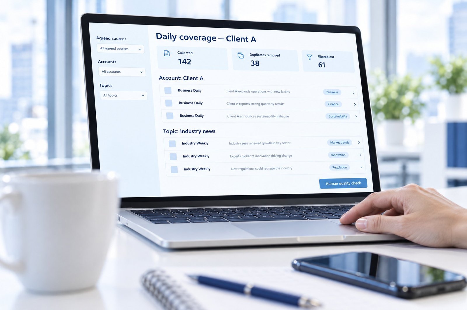 Close-up of a laptop showing a media monitoring dashboard for Client A: coverage collected, duplicates removed and results filtered out, grouped by account and topic, with a human quality check button; a coffee cup, phone and notebook sit in the foreground
